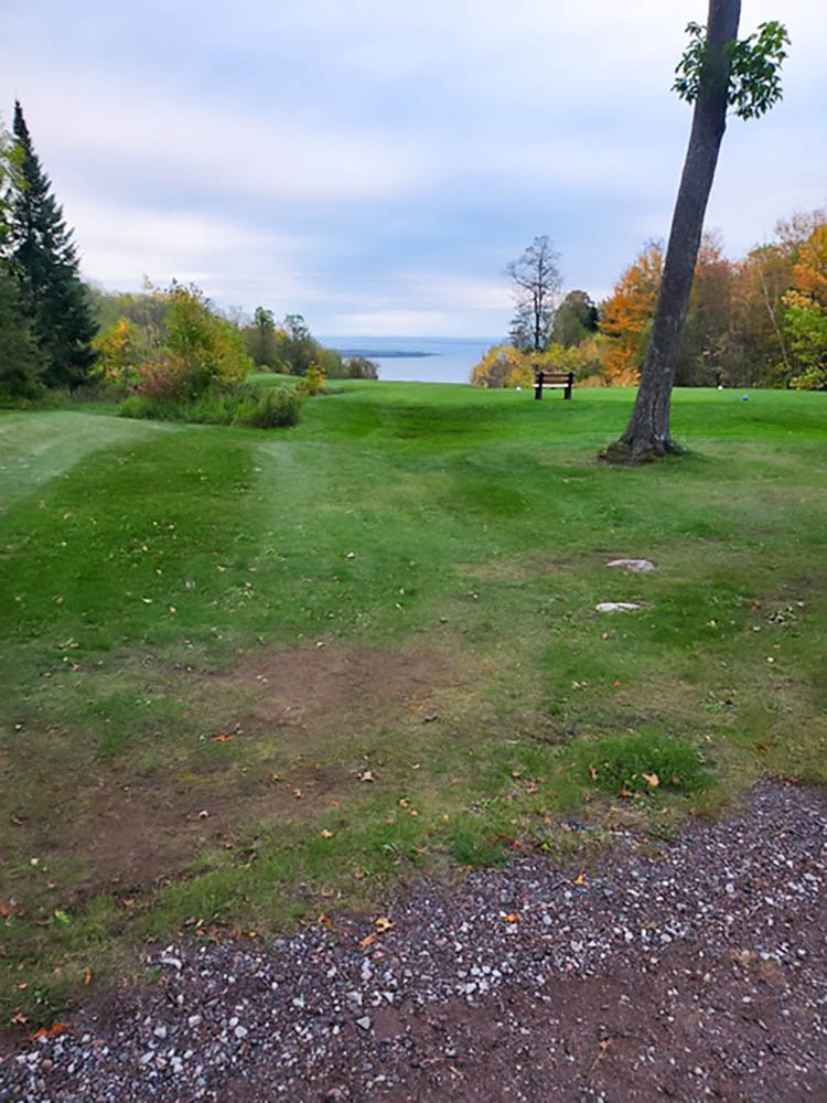View across a fairway of green grass with Lake Superior in the far distance.