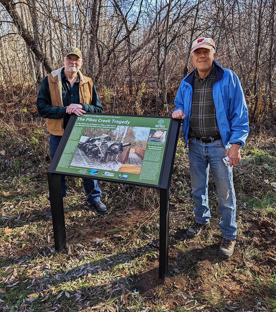 Two men standing by an informational sign along a trail.