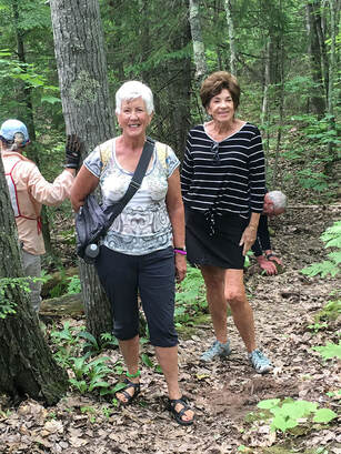 Two women standing on a trail in the forest.