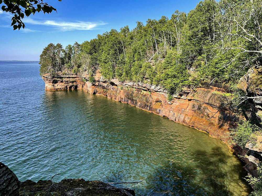 View across blue water with sandstone cliffs topped by a green forest